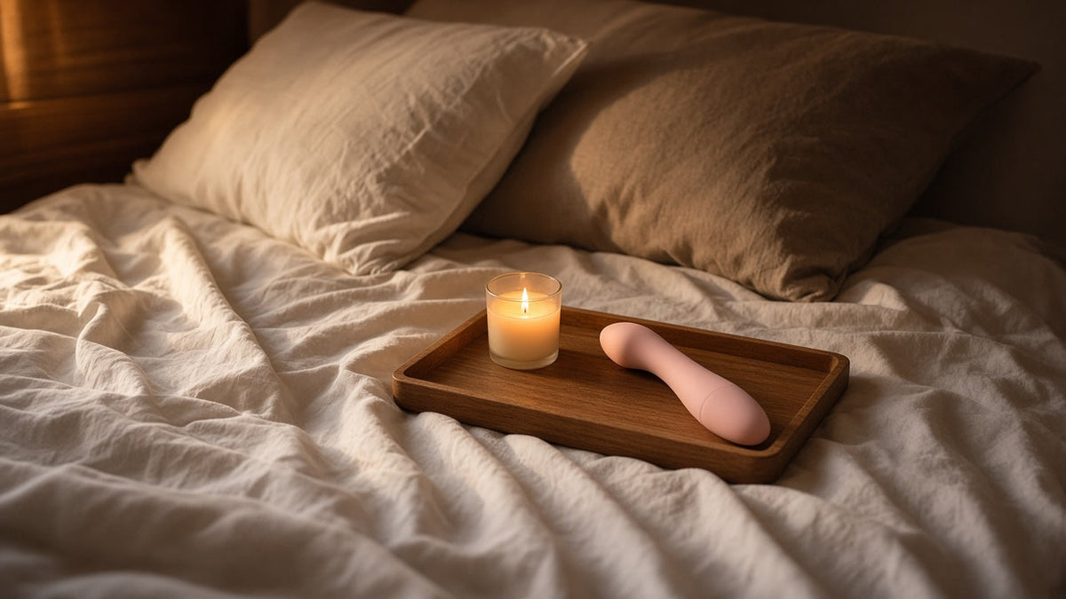 Cama con sábanas de lino, vela y juguete de silicona rosa sobre una bandeja de madera